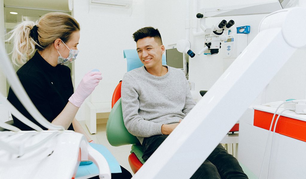 A man, smiling, sitting in a dentist chair besides the dentist.